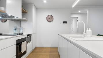 A modern kitchen with white cabinetry, a built-in oven, a microwave, and a stainless steel range hood.