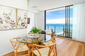 A dining area with a glass table and wicker chairs, a potted plant, and a view of the ocean through a sliding glass door. - Perfect Penthouse - WiFi included - No Airbnb Fees (Newcastle)