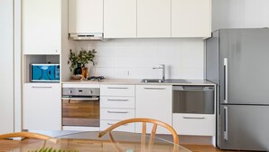 Une cuisine moderne avec des armoires blanches, un réfrigérateur en acier inoxydable, un four encastré et un évier.