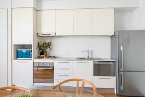 Una cocina moderna con armarios blancos, un refrigerador de acero inoxidable, un horno empotrado y un lavamanos.