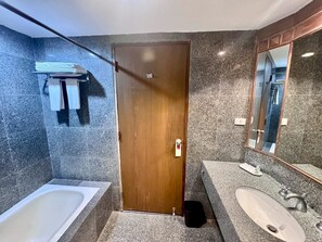 A bathroom with a wooden door, a bathtub, a sink, and a mirror. - AMIS By Sima Thani (Nakhon Ratchasima)