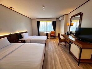 A hotel room with two beds, a desk with a TV, a chair, and a window with curtains. - AMIS By Sima Thani (Nakhon Ratchasima)