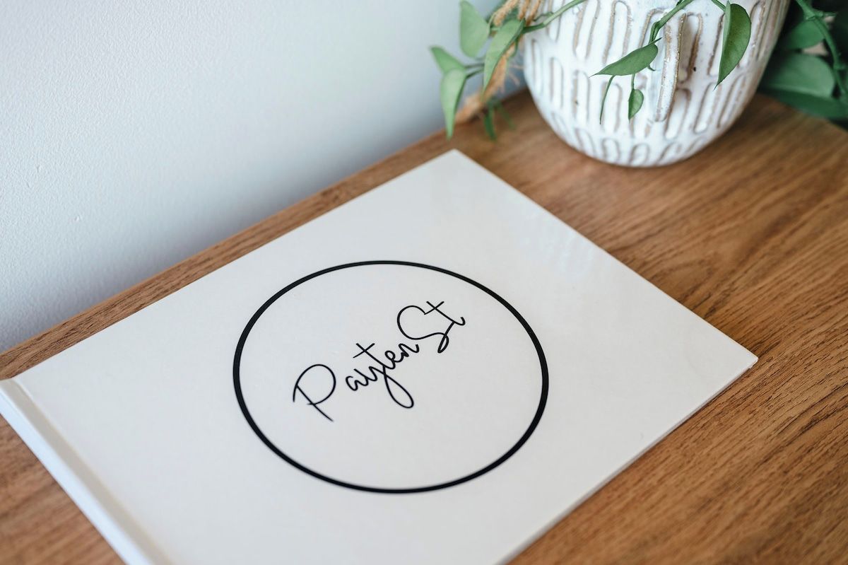 Een wit boekje met 'Payten St' in een cirkelvormig ontwerp op een houten ondergrond.