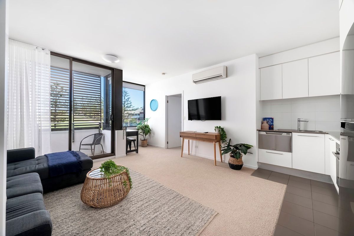 A modern living room with a sofa, a coffee table, and a TV. There is a sliding glass door leading to a balcony.