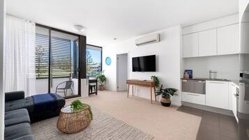 A modern living room with a sofa, a coffee table, and a TV. There is a sliding glass door leading to a balcony.