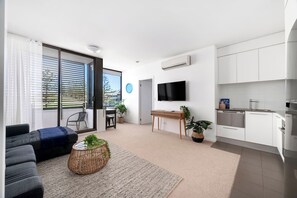 A modern living room with a sofa, a coffee table, and a TV. There is a sliding glass door leading to a balcony. - Amazing Apartment - No Platform Fees - Free Wi-Fi (Newcastle)