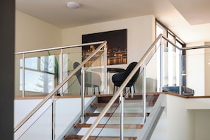 Una escalera moderna con barandillas de cristal y peldaños de madera que conduce a un comedor con mesa y sillas.
