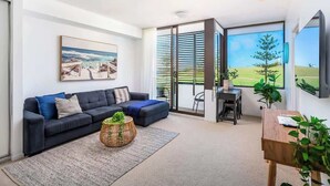 Un salon moderne avec un canapé bleu foncé, une table basse en osier et un tableau représentant une scène de plage.