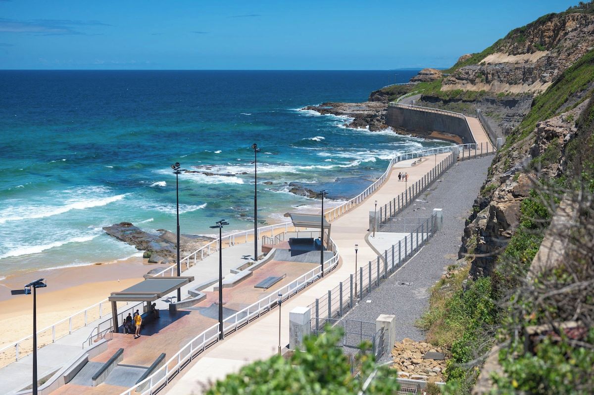 A coastal walkway with a curved path, benches, and a viewing area overlooking the ocean.