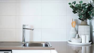 Una cocina con un lavamanos de acero inoxidable, una llave moderna y un salpicadero blanco de azulejos.