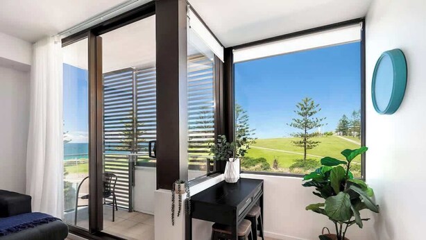 Une chambre moderne dotée d’une porte-fenêtre coulissante donnant sur un balcon, d’une table à manger noire, d’une plante en pot et offrant une vue sur un paysage verdoyant.