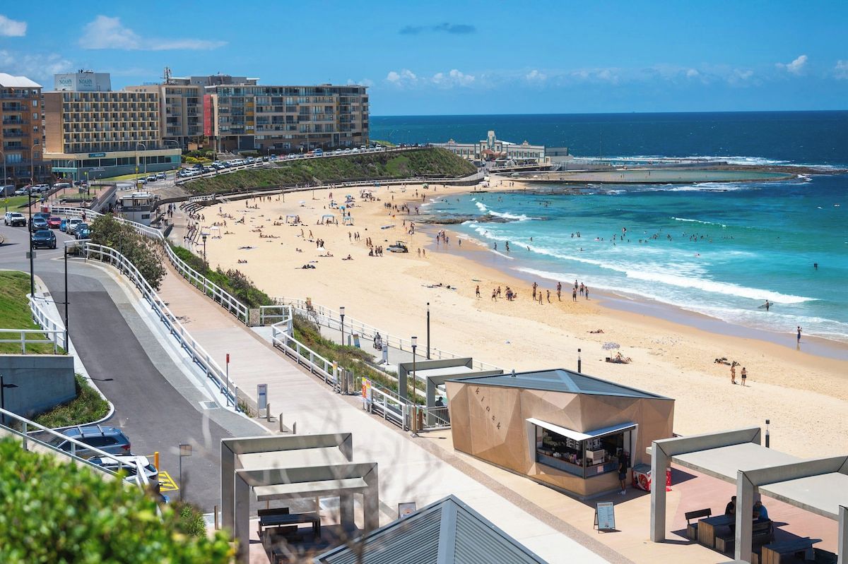 A coastal hotel with a beach view, a parking area, and a promenade.