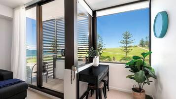 A modern room with a sliding glass door leading to a balcony, a black desk, a potted plant, and a view of a green landscape.