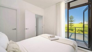 Une chambre d’hôtel avec un lit, une vue sur un paysage verdoyant par une grande fenêtre et une porte donnant sur une autre pièce.