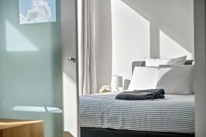 A modern bedroom with a bed, pillows, a bedside table, and a window with curtains.