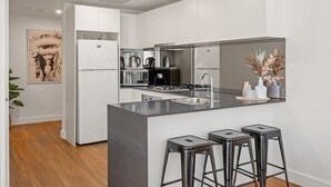 Une cuisine moderne avec des meubles blancs, un îlot central doté de tabourets, un réfrigérateur en acier inoxydable et une machine à café.