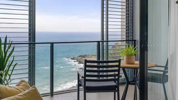 A balcony with a view of the ocean, a chair, a small table, and a potted plant.