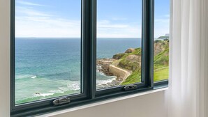 A coastal view through a window with a view of the ocean, cliffs, and a paved path.