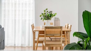 A dining area with a wooden table, chairs, a vase with green plants, and a window with sheer curtains. - Enjoyable East End (Newcastle)