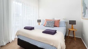 A bedroom with a bed, pillows, a bedside table, a lamp, and a window with curtains. - Enjoyable East End (Newcastle)