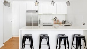 A modern kitchen with white cabinets, stainless steel appliances, and black bar stools. - Enjoyable East End (Newcastle)