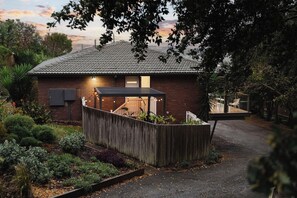 Una casa con techo inclinado, un jardín cercado y un espacio de estar cubierto al aire libre.