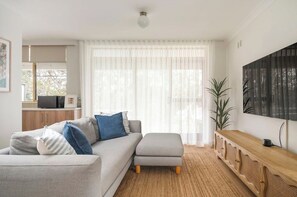 A modern living room with a grey sectional sofa, a wooden console table, and a large window with sheer curtains.