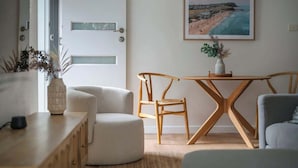 A modern living room with a wooden dining table, two chairs, a sofa, and a framed beach painting on the wall. - Bar Beach Bliss - 10 min walk to the Beach (Bar Beach)