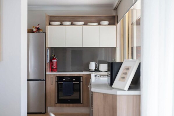 Cocina compacta con horno integrado, cafetera y un cuadro en la encimera.