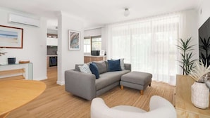A modern living room with a grey sectional sofa, a wooden dining table, and a white armchair. - Bar Beach Bliss - 10 min walk to the Beach (Bar Beach)