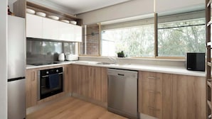 A modern kitchen with wooden cabinets, a built-in oven, a dishwasher, and a window with a view of trees. - Bar Beach Bliss - 10 min walk to the Beach (Bar Beach)