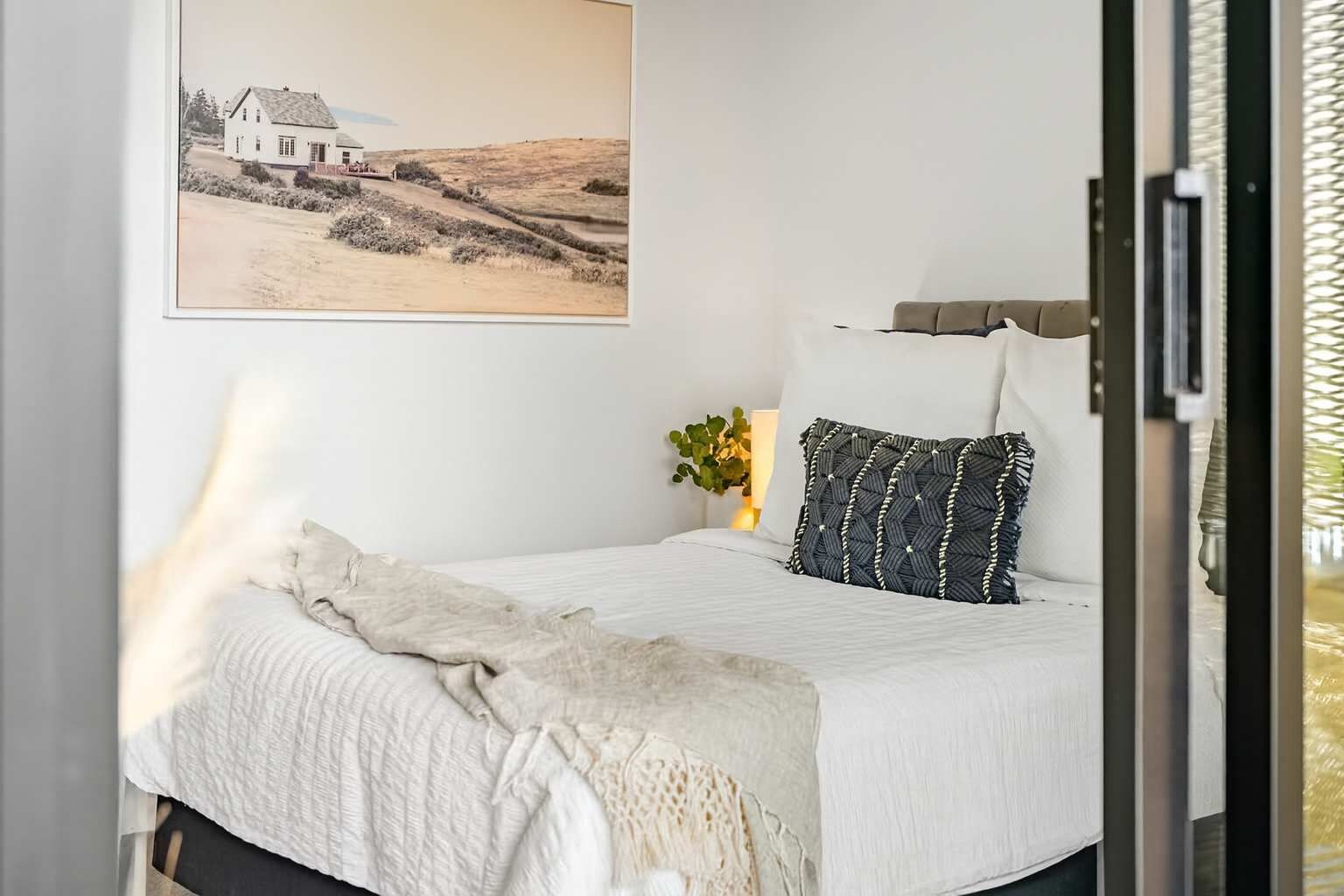 A bedroom with a bed, a pillow, a blanket, a wall-mounted picture, and a bedside lamp.