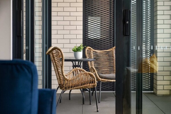 A modern outdoor seating area with wicker chairs and a small table, a potted plant, and a glass partition.