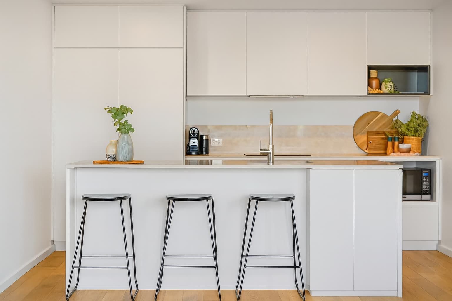 A modern kitchen with white cabinetry, a central island with stools, a coffee machine, and a microwave.
