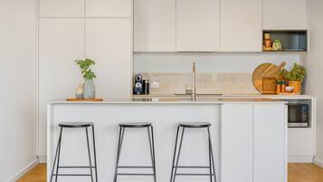A modern kitchen with white cabinetry, a central island with stools, a coffee machine, and a microwave.