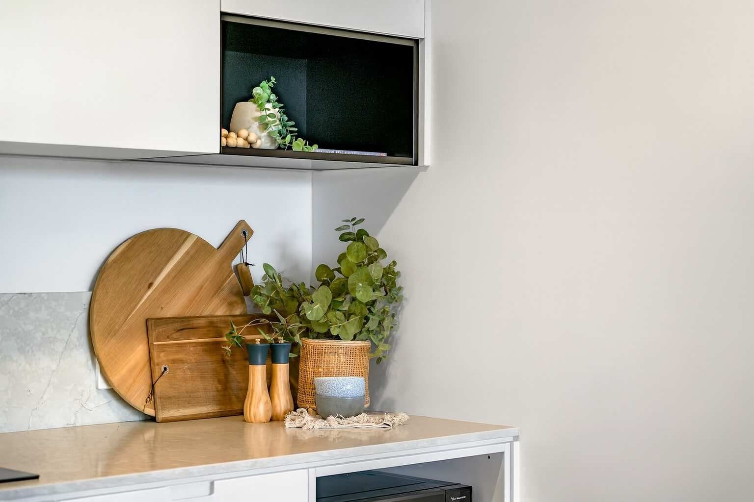 A kitchen counter with a wooden cutting board, a plant, and two spice containers.