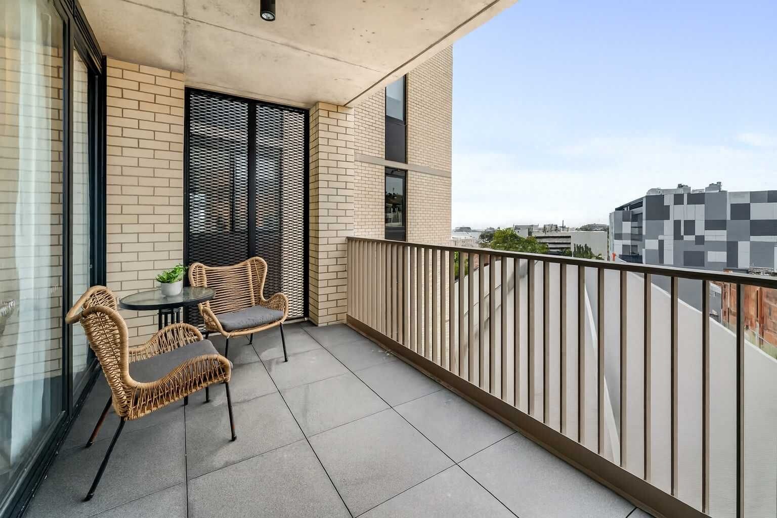A balcony with wicker furniture and a potted plant, a brick wall, and a view of the cityscape.