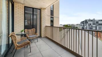 A balcony with wicker furniture and a potted plant, a brick wall, and a view of the cityscape.