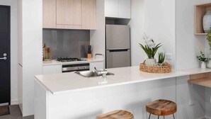Una cocina moderna con armarios blancos, un refrigerador de acero inoxidable, una estufa a gas y una isla central con taburetes.