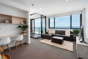 A modern living room with a large window, a sofa, a coffee table, and a desk with chairs.