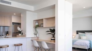 Una cocina moderna con taburetes de bar, un comedor con mesa de madera y un dormitorio con cama y mesita de noche.