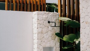 Un espacio exterior moderno con pared de piedra, listones de madera y abundante vegetación.