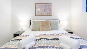 A neatly made bed with patterned bedding and two rolled towels on it.