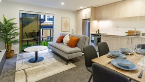 A modern living room with a sofa, dining table set for four, and a kitchen area with wooden cabinets.