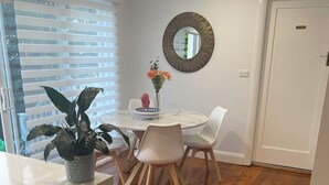 A dining area with a round table, white chairs, a potted plant, and a mirror on the wall.