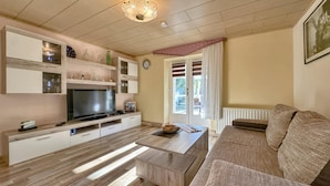 Een moderne woonkamer met een flatscreen televisie, houten kasten, een bank en een eethoek.