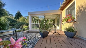 Een houten terras met planten in potten en een glazen deur die naar een kamer leidt.