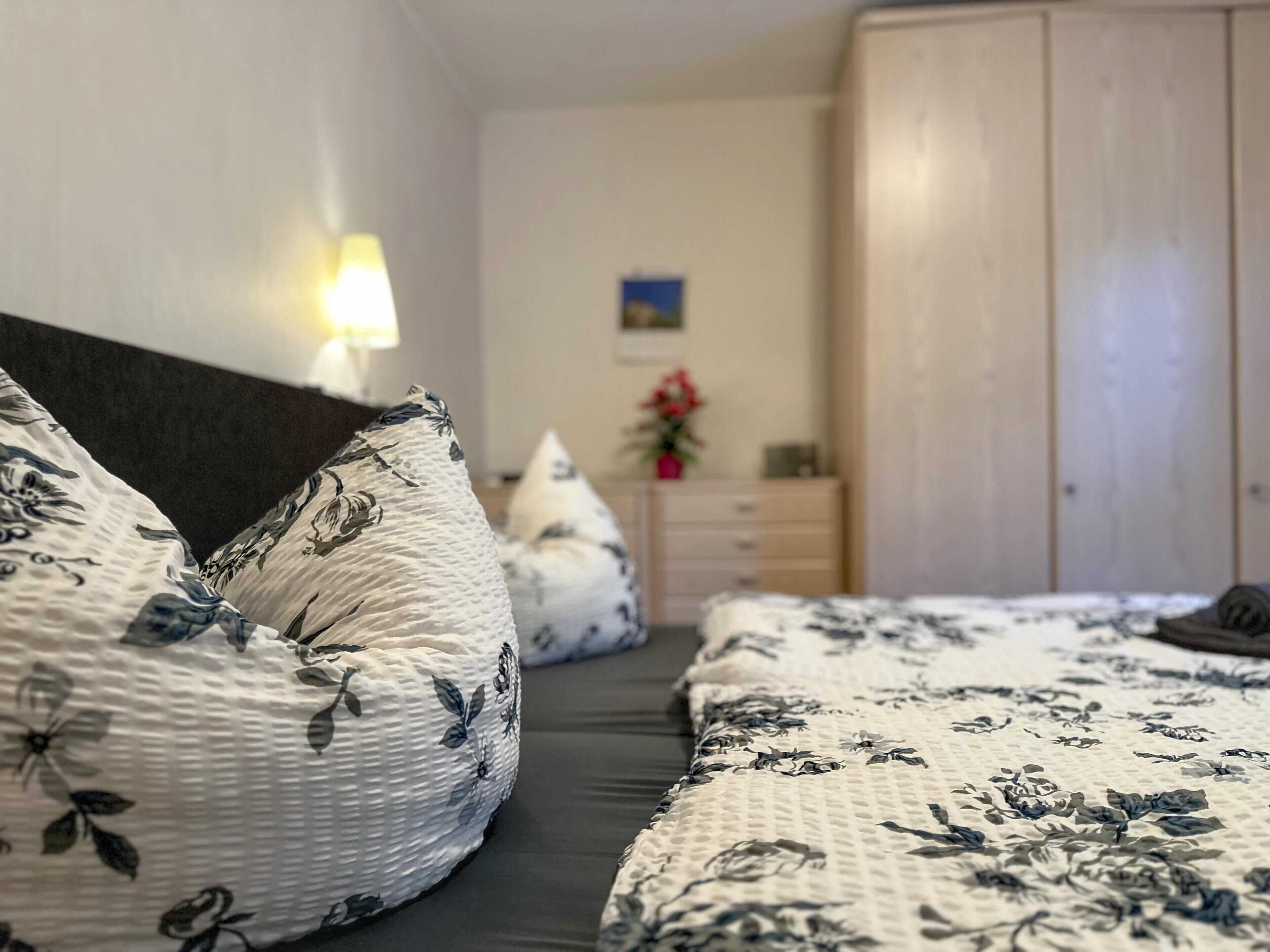 A bedroom with a bed, pillows, a nightstand, a dresser, and a lamp.
