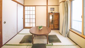 Une pièce de style japonais traditionnel, avec un sol recouvert de tatamis, une table en bois avec des coussins, un ventilateur de plafond et une porte coulissante.