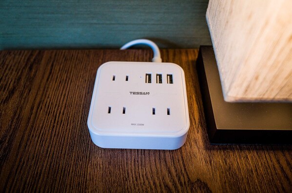 A white Tessan power strip with four USB ports and a label indicating a maximum of 1500W on a wooden surface.